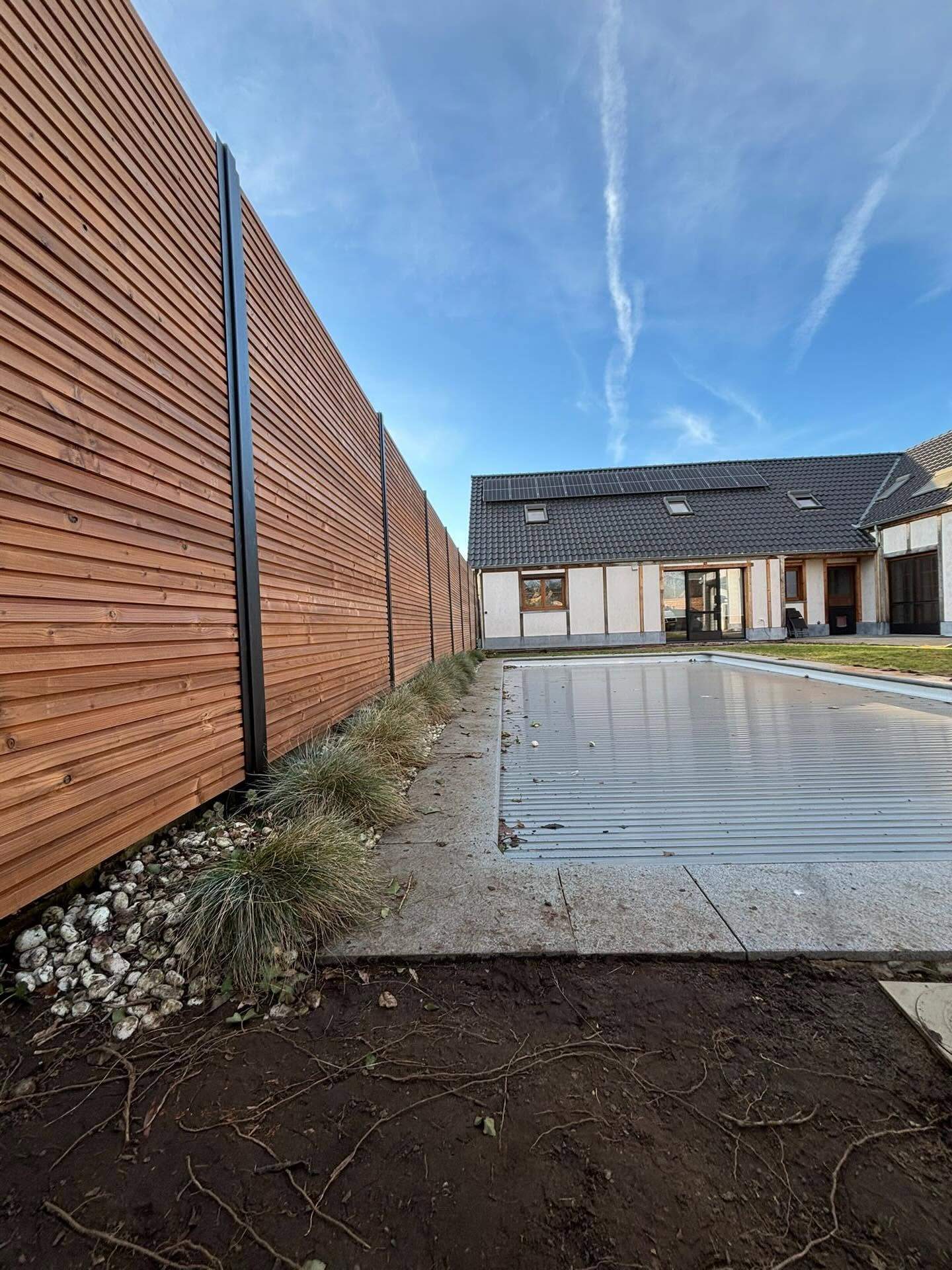 Houten hekwerk met fijne lamellen op zwarte stalen palen rond een nieuwbouwwoning met zwembad in Alken