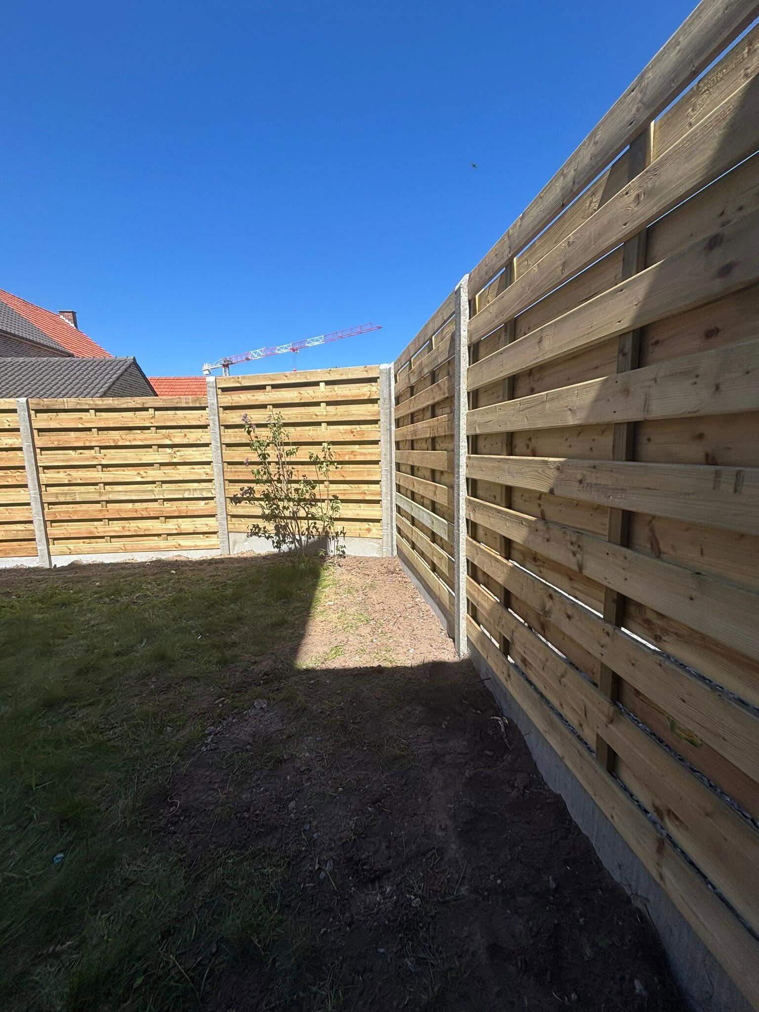 Houten schutsels op betonpalen rond een nieuw aangelegde tuin.