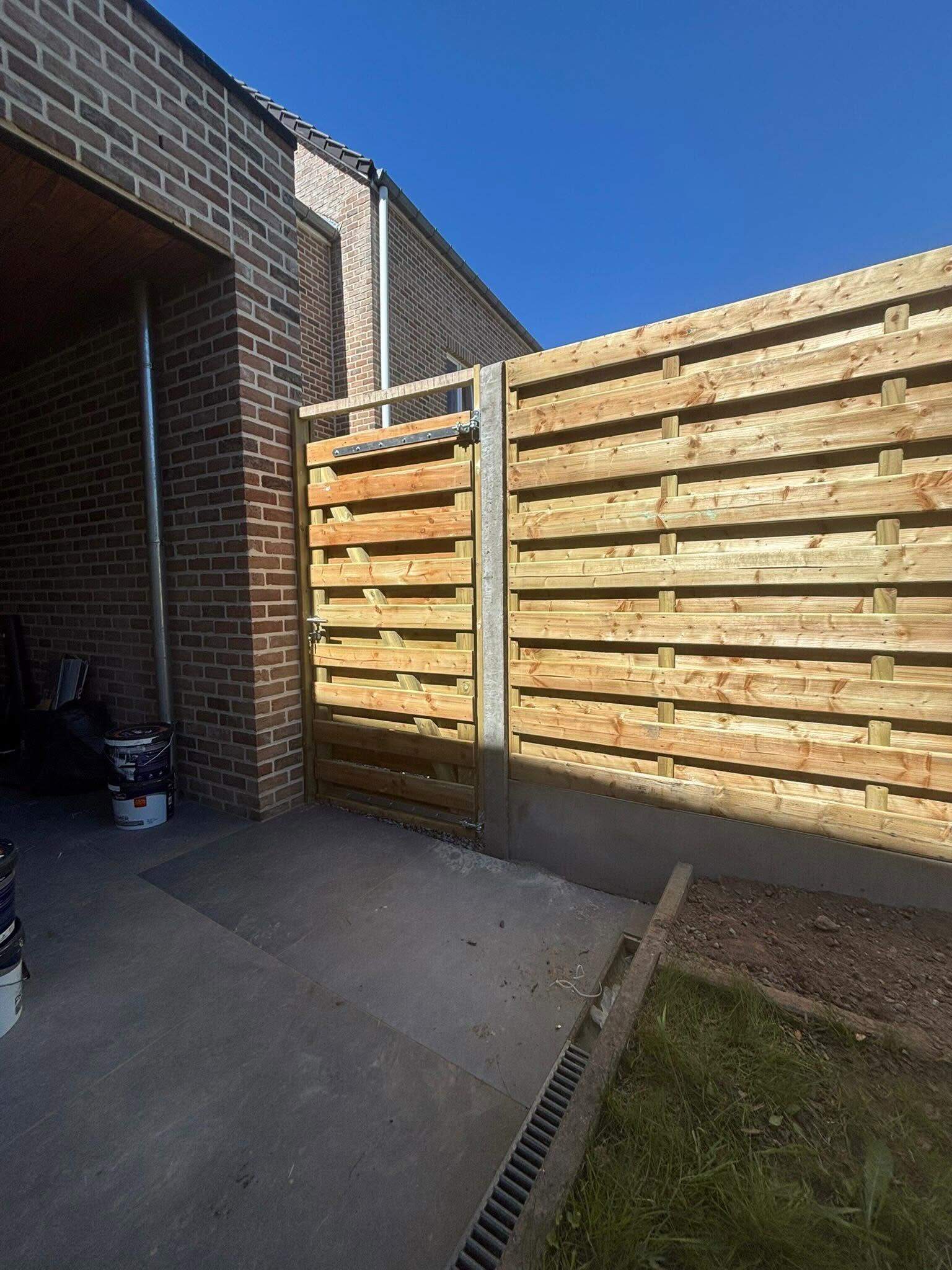 Houten tuinpoortje naast een houten schutsel op betonpalen bij een woning in Gingelom