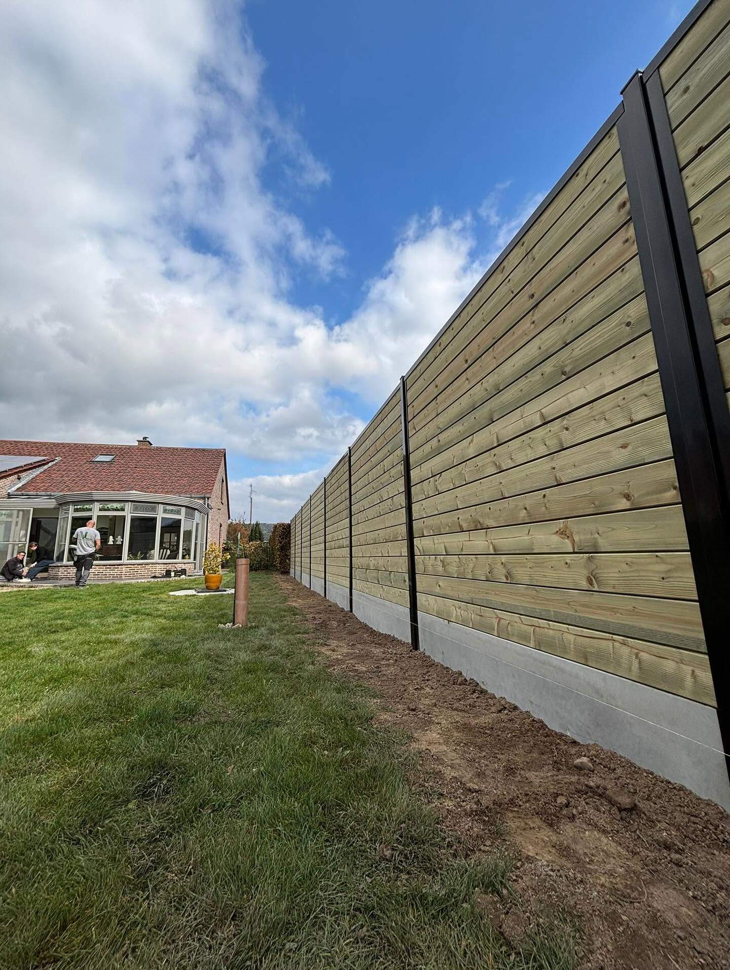 Lange rij houten schutsels op een betonnen onderplaat langs een tuin in Lubbeek