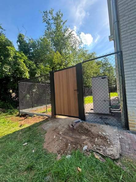 Poort met houten vulling in een zwart kader, naast de draadafsluiting.