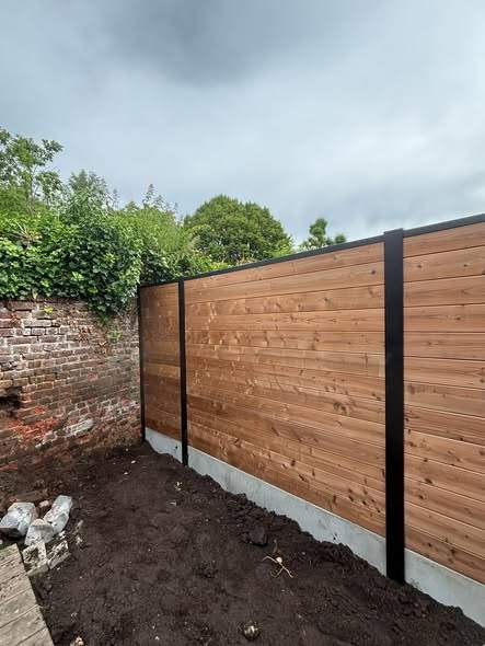 Thermowood op aluminium palen, tegen de oude tuinmuur.