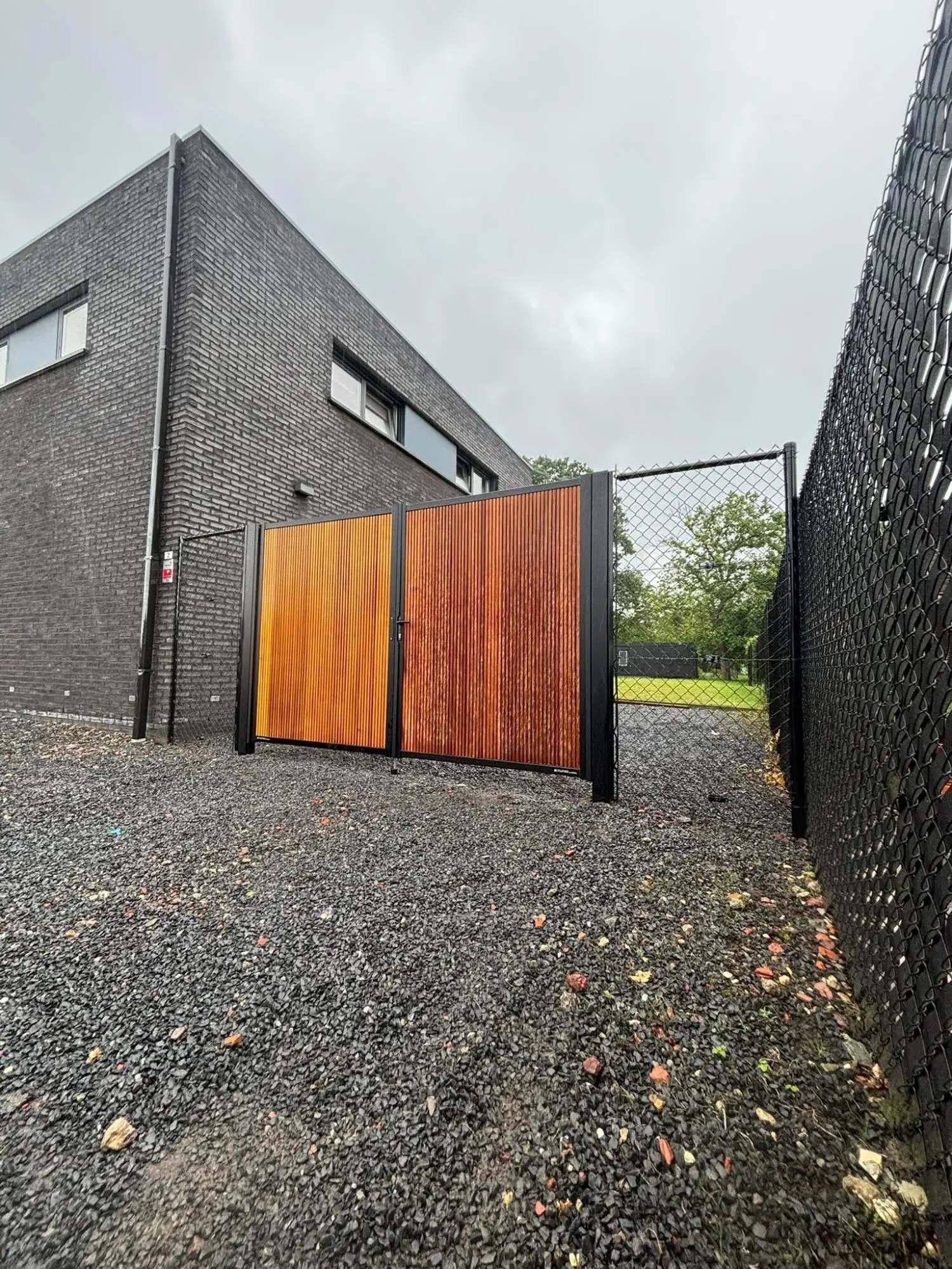Houten poort op maat tussen zwarte stalen kaders, geplaatst bij een bedrijfspand